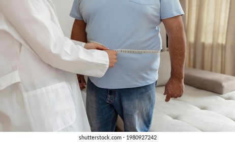 A Nutritionist Doctor Measures The Body Of A Male Patient With A Measuring Tape On Adipose Tissue And Excess Weight. Overweight Obesity Man Seeing Doctor For Treatment Of His Illness And Weight Loss.