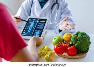 nutritionist female doctor using digital mobile tablet with virtual graphic icon diagram and vegetable and fruit with patient on desk at office hospital, nutrition, food science, healthy food concept