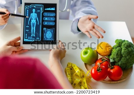 nutritionist female doctor using digital mobile tablet with virtual graphic icon diagram and vegetable and fruit with patient on desk at office hospital, nutrition, food science, healthy food concept