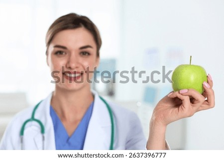 Nutritionist with green apple and stethoscope in clinic, selective focus