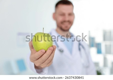 Nutritionist with green apple and stethoscope in clinic, selective focus