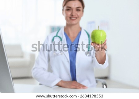 Nutritionist with green apple and stethoscope at table in clinic, selective focus