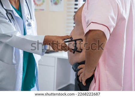 Nutritionist hand using measuring body fat with caliper device to measure belly of obese elderly male patient for obesity treatment and dieting in hospital
