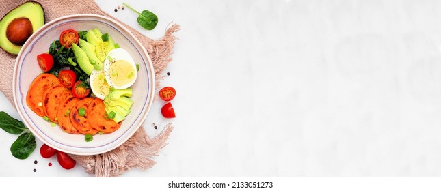 Nutritious breakfast bowl with sweet potato, egg, avocado and spinach. Overhead view table scene on a white marble banner background. Copy space.