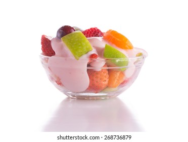 Nutritious breakfast with fruit salad topped with pink strawberry yogurt in a glass bowl, on white background