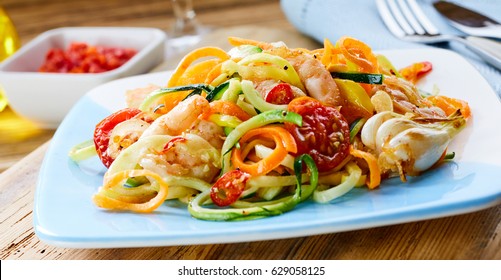 Nutritious healthy prawn appetiser with diced fresh raw vegetable salad seasoned with black pepper and olive oil viewed low angle from the side on a blue plate