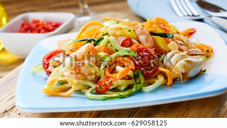 Nutritious healthy prawn appetiser with diced fresh raw vegetable salad seasoned with black pepper and olive oil viewed low angle from the side on a blue plate