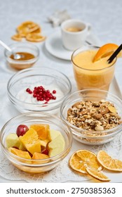 A nutritious set of breakfast items including a fruit bowl, granola, yogurt with berries, orange smoothie, and espresso are arranged on a white table.