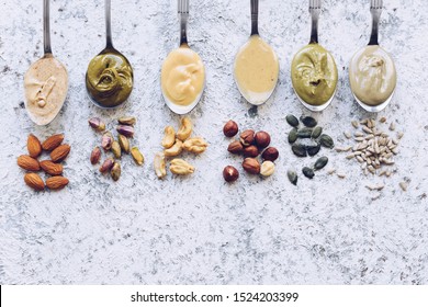 Nuts and seeds butter on a spoons with ingredients. Homemade raw organic almond, hazlenut, cashew, pistachio nuts paste and sunflower and pumpkin seeds butter. Top view. Copy space.