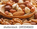 Nuts and seeds of different types with a wooden spoon closeup with selective focus - peeled walnut, hazelnuts, peeled peanut, pine nut kernels, almond seeds, cashew seeds, pistachio nuts in the shell