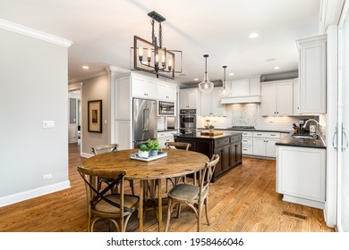 OAK PARK, IL, USA - APRIL 19, 2020: A Modern Farmhouse Kitchen With White Cabinets And A Dark Wood Island. A Chandelier Hangs Above A Large Wooden Table On Hardwood Floors.