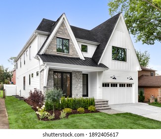 OAK PARK, IL, USA - AUGUST 17, 2020: A New, White Modern Farmhouse With A Dark Shingled Roof And Black Windows. The Left Side Of The House Has A Light Rock Siding And A Covered Front Porch.