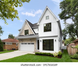 OAK PARK, IL, USA - AUGUST 17, 2020: A new, white modern farmhouse with a dark shingled roof and black windows. The left side of the house is covered in a rock siding.