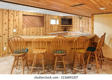 OAK PARK, IL, USA - JUNE 18, 2021: A Basement Wet Bar With Wood Walls, Bar And Stools. A Television Is Mounted On The Wall Behind The Bar.