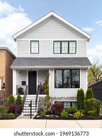 OAK PARK, IL, USA - MARCH 1, 2021: A Beautiful, Modern Farmhouse Surrounded By A Black Wrought Iron Fence With Bushes And Plants Behind. Stairs Lead To A Black Front Door.