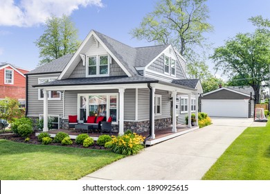 OAK PARK, IL, USA - MAY 28, 2020: The exterior of a grey modern, suburban home with a covered porch and furniture featuring red accent pillows. 