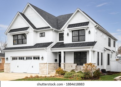 OAK PARK, IL, USA - NOVEMBER 2, 2020: A new, white modern farmhouse with a dark shingled roof and black windows. The bottom of the house has a light rock siding and a covered front porch.