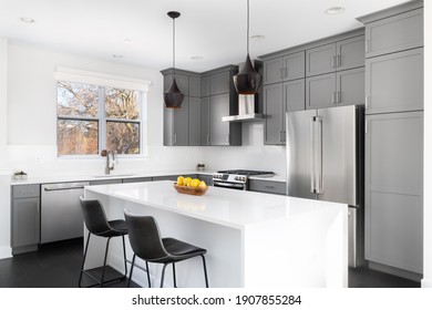 OAK PARK, IL, USA - NOVEMBER 1, 2020: A Modern Kitchen With Grey Cabinets, A Bowl Of Lemons On The White Granite Counter Tops, And Dark Hardwood Floors.