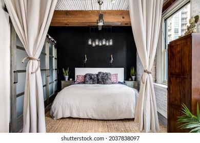 OAK PARK, IL, USA - NOVEMBER 2, 2020: A Bedroom In A Loft Condo With An Exposed Wood Ceiling, Glass Sliding Doors To A Closet, Black Accent Wall, And A Fancy Glass Light Hanging Above.