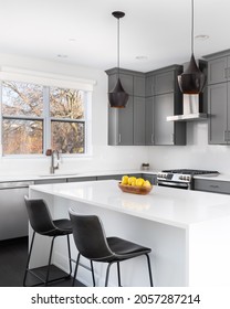 OAK PARK, IL, USA - NOVEMBER 1, 2020: A Modern Kitchen With Grey Cabinets, A Bowl Of Lemons On The White Granite Counter Tops, And Dark Hardwood Floors.