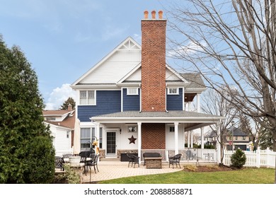 OAK PARK, IL, USA - NOVEMBER 1, 2021: The Back Patio Of A Blue And White Modern Farmhouse With A Stone Patio, Covered Porch, And A Brick Chimney.