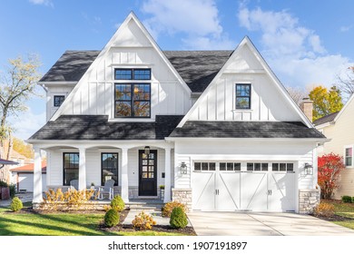 OAK PARK, IL, USA - OCTOBER 28, 2020: A new, white modern farmhouse with a dark shingled roof and black window frames. The bottom of the house has a light rock siding and covered front porch.