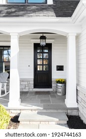 OAK PARK, IL, USA - OCTOBER 28, 2020: A New, White Modern Farmhouse With A Dark Wood Door With Windows, White Pillars, A Stone Floor, And Patio Furniture.