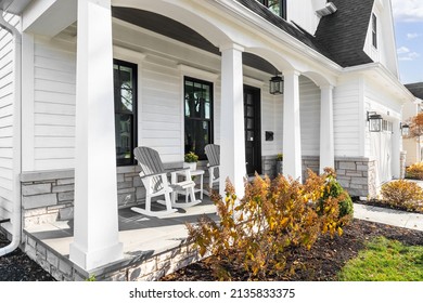 OAK PARK, IL, USA - OCTOBER 28, 2020: A New, White Modern Farmhouse With A Dark Wood Door With Windows, White Pillars, A Stone Floor, And Patio Furniture.