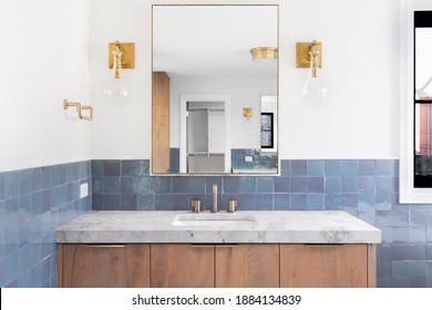 OAK PARK, IL, USA - SEPTEMBER 15, 2020: A Luxury Home's Renovated Bathroom With Blue Tiles, A Light Wood Vanity Cabinet, Gold Lights Mounted On The Wall, And A Grey Stone Counter Top.