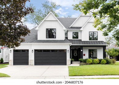 OAK PARK, IL, USA - SEPTEMBER 12, 2021: A luxury, white modern farmhouse with black framed windows, garage doors, and covered porch.