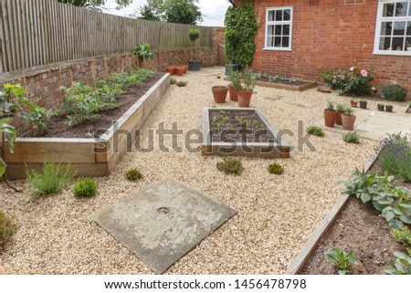 Oak sleeper raised beds in a courtyard garden design with hard landscpaing, gravel and terracotta pots