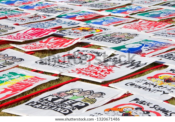 Oakland, CA - February 22, 2019: Oakland teachers\
strike day 2 rally at DeFremery Park, then marching downtown..\
Fighting for smaller class sizes and bigger paychecks. Signs laying\
on grass
