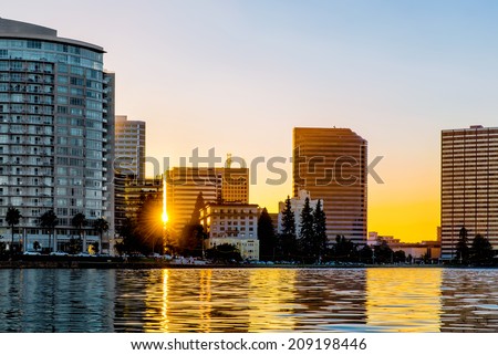 Oakland Lake Merritt waterfront buildings backlit at sunset with sun flare and reflections on the lake. Viewed from the water. Copy space.