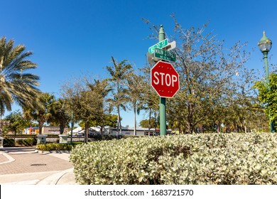 Oakland Park, Florida / USA - 1/21/2019: Stop Sign And Street Designation On The Corner Of NE 32 Street And Main Street NE 12 Avenue Intersection With Strip Mall And Businesses Behind Street And Hedge