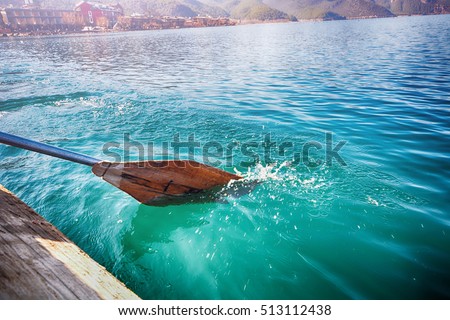 Oar of boat touching water and causing splash and ripples in the water.