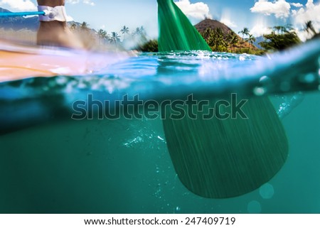 Oar of paddle boarder half way submerged in ocean water paddling