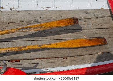 Oars laying in bottom of rowing boat on wooden plank floor, inside view of traditionally built rowing boat, red and white colour, old boat in sunny weather close up shot. - Powered by Shutterstock