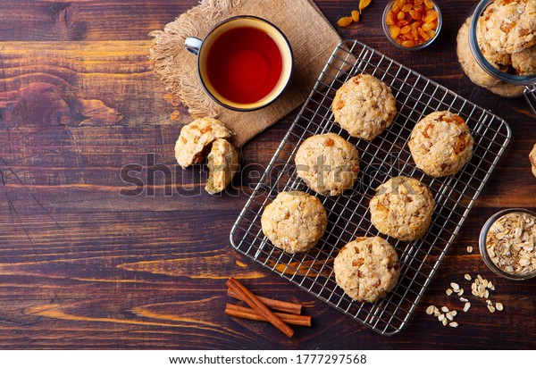 Oat vegan cookies on cooling rack\
with cup of tea. Wooden background. Copy space. Top\
view.