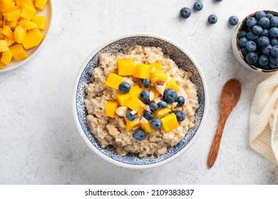 Oatmeal bowl with mango and blueberries on grey concrete background, table top view - Shutterstock ID 2109383837