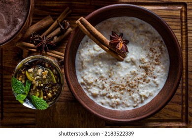 Oatmeal with cinnamon, cinnamon stick, cardamom in a ceramic, brown bowl, on a wooden board. On the board are cinnamon sticks and cardamom stars, a cup of cocoa and an iron bowl of lime and orch  - Powered by Shutterstock