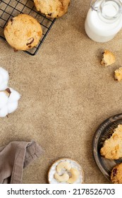 Oatmeal Cookies With Cranberry, Cashew And White Chocolate. Bottle Of Milk, Cooling Rack With Cookies, Kitchen Towel, Nuts And Cotton Flower. Brown Background, Space For Text. Food Frame