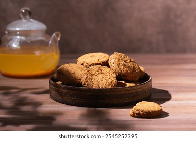 Oatmeal cookies in a plate with sea buckthorn tea in a teapot on a wooden table. Hard light. - Powered by Shutterstock