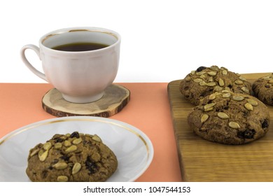 Oatmeal Cookies With Raisins And Sunflower Seeds On A Bamboo Board, On The Left A Mug With Tea On A Wooden Stand, One Cookie In A Saucer, Side View, On An Orange Table,  Isolated On A White Background