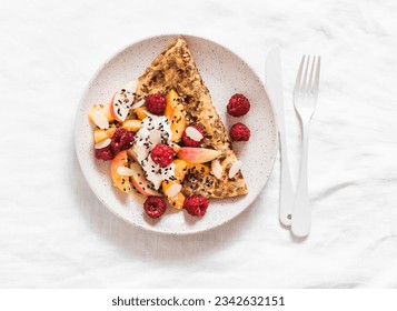 Oatmeal pancake made of whole grain flakes and eggs with fruits, berries and Greek yogurt on a light background, top view   