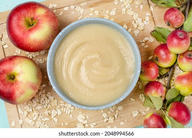 Oatmeal Porridge For The Baby From Ground Cereals In A Blue Bowl, Red Ripe Apples On A Wooden Board Close-up. The First Complementary Food Of A Child, Baby Nutrition.