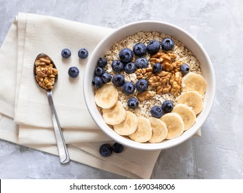Oatmeal. Porridge with bananas, blueberries and walnut for healthy breakfast or lunch. Natural ingredients. Flat lay design on linen napkin and cement background