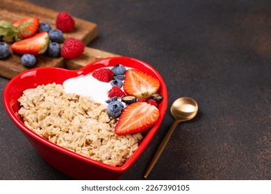Oatmeal porridge with berry and yogurt in red bowl in the heart shape, top view. Oat flakes healthy breakfast meal. Clean eating, dieting, healthy food. Copy space