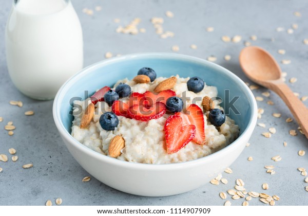 Oatmeal porridge in a blue bowl\
with berries and nuts. Porridge oats bowl with strawberries\
blueberries and almonds. Healthy eating, dieting, vegetarian food\
concept