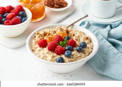 Oatmeal Porridge With Blueberry, Raspberries, Jam And Nuts In White Bowl, Dash Diet With Berries, White Background, Side View. Healthy Diet Breakfast