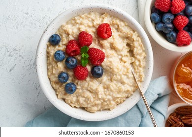 Oatmeal Porridge With Blueberry, Raspberries, Jam And Nuts In White Bowl, Dash Diet With Berries, White Background, Top View Copy Space. Healthy Diet Breakfast